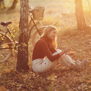 Happy active young woman riding vintage bicycle in autumn park at sunset