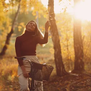 Happy active young woman riding vintage bicycle in autumn park at sunset
