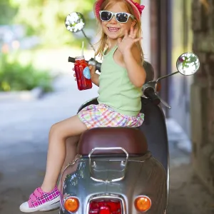Happy little girl sitting in a vintage scooter in the street wearing hat and sunglasses drinking juice Happy little girl sitting in a vintage scooter in the street wearing hat and sunglasses drinking juice