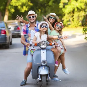 Happy young family riding a vintage scooter in the street wearing hats and sunglasses Happy young family riding a vintage scooter in the street wearing hats and sunglasses