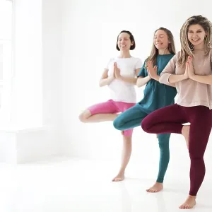 Happy young women smiling meditating against white wall during yoga session Happy young women smiling meditating against white wall during yoga session