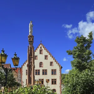 Bâtiment historique avec statue et colonne entouré d'arbres sous un ciel bleu.