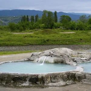 Hot spring pool surrounded by green landscape and forested mountains in the background