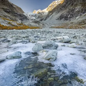 Ice structures on mountain stream with autumnal larches and mountain panorama