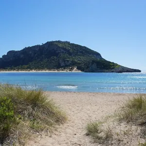 An idyllic beach with clear blue water and a mountain in the background on a sunny day An idyllic beach with clear blue water and a mountain in the background on a sunny day