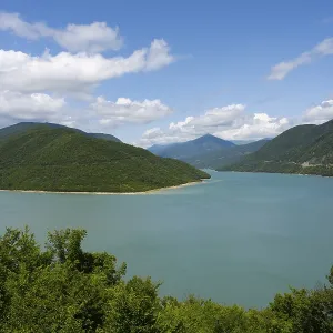 Idyllic landscape with a large lake surrounded by green mountains under a blue sky with clouds