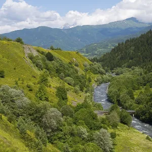 Idyllic landscape with a river flowing through green mountains and forests under clear skies
