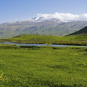 Idyllic landscape with snow-covered mountains and green grass under a blue sky Idyllic landscape with snow-covered mountains and green grass under a blue sky
