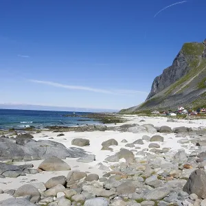 An idyllic sandy beach with rocks and clear water against a backdrop of mountains and blue skies Vikten Lofoten
