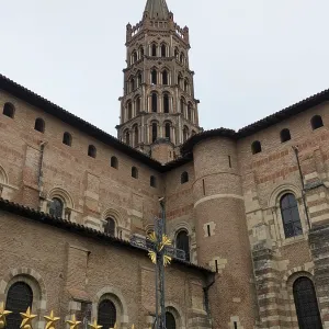 Imposing historic structure with a tall Romanesque tower and brick facade under a cloudy sky