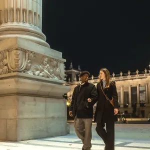 Interracial couple strolling arm in arm past an illuminated historic monument at night Interracial couple strolling arm in arm past an illuminated historic monument at night