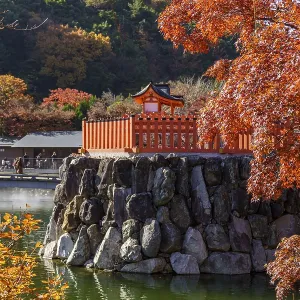 Japanese temple in autumn with bright red leaves and reflection in calm water