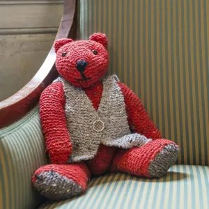 Knitted red teddy bear with vest on striped armchair
