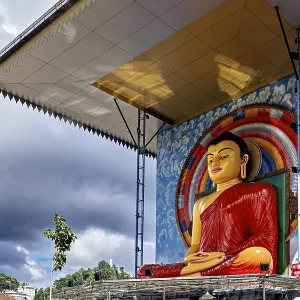 Large Buddha statue under a roof surrounded by rainbow and cloudy sky
