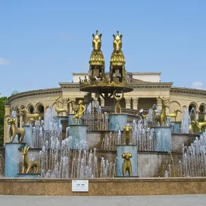 Large fountain with golden statues in an architectural and green setting