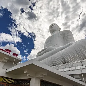 Large white Buddha statue under dramatic sky surrounded by temple architecture and clouds