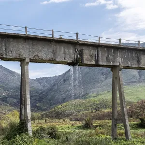 Leaky aqueduct with waterfall against mountain backdrop