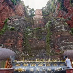 Leshan, China - July 2019 : Chinese male pilgrim lightening memorial candles at the bottom of The Giant Leshan Buddha