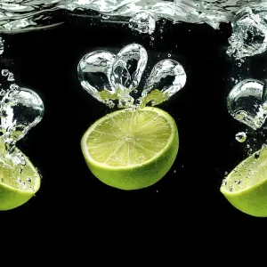 Three lime halves, splashing into water against black