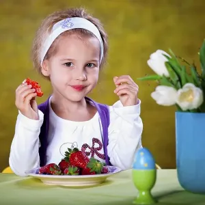 Little blonde girl eating strawberries at a table