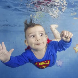 Little boy in a superman costume dives underwater in the pool