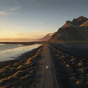 A lone car travels down a long dirt road flanked by dramatic mountainous terrain at sunset A lone car travels down a long dirt road flanked by dramatic mountainous terrain at sunset