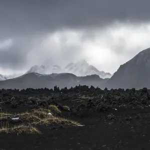 Vue panoramique majestueuse des hautes terres d'Islande avec un terrain volcanique et des sommets recouverts de neige à l'horizon sous un ciel maussade.
