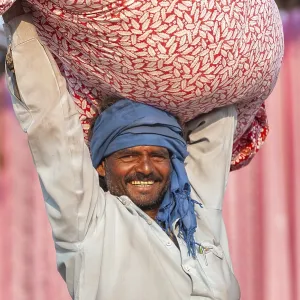 Man carrying a bundle of cloth on his head in front of pink fabric panels Man carrying a bundle of cloth on his head in front of pink fabric panels