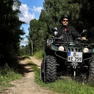 Man rides ATV on a forest trail surrounded by tall vegetation