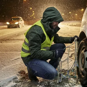 Man with safety vest applying snow chains on snow-covered road