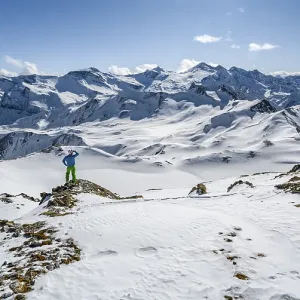 Man, ski tourer looks over snow-covered mountain ranges