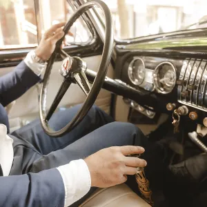 A man in a suit is driving a car with a black steering wheel