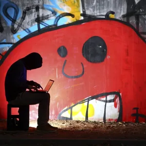 Man surfing on a laptop computer in front of a graffiti covered wall