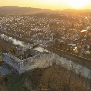 Medieval ruin on a river, with illuminated cityscape at dusk