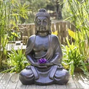 Meditating Buddha Statue with a purple lotus on his hands on a backyard