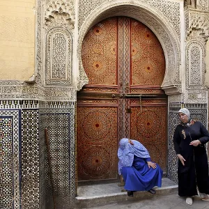 Two men in front of an artfully decorated wooden door with mosaic decoration