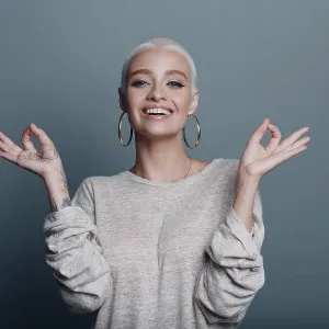 Millenial young woman with short blonde hair portrait sitting and meditate with ok sign mudra on gray blue background Millenial young woman with short blonde hair portrait sitting and meditate with ok sign mudra on gray blue background