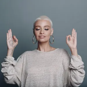Millenial young woman with short blonde hair portrait sitting and meditate with ok sign mudra on gray blue background Millenial young woman with short blonde hair portrait sitting and meditate with ok sign mudra on gray blue background