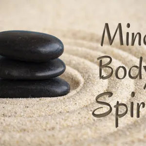 Mind, body and spirit text with black Zen stones on sand background