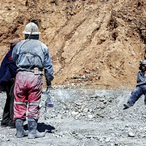 Miners in different clothes stand or sit in a barren
