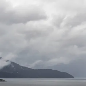 A misty lake with distant mountains and overcast clouds creating a serene