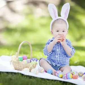 mixed-race chinese and caucasian baby boy outside wearing rabbit ears playing with easter eggs mixed-race chinese and caucasian baby boy outside wearing rabbit ears playing with easter eggs