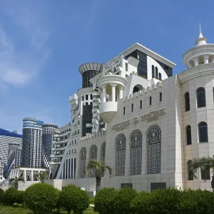 A modern building with an elegant design surrounded by palm trees and green spaces under a blue sky