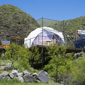 A modern dome tent in a mountainous landscape under blue sky