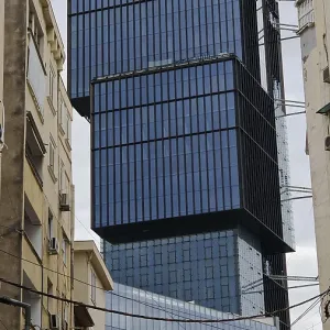 Modern high-rise building with glass facade between older buildings in an urban environment under cloudy sky