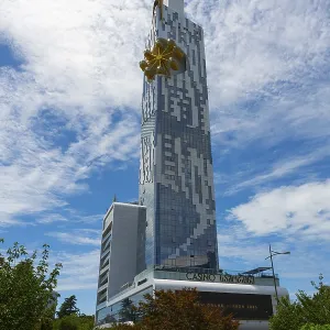 A modern high-rise building rises against a blue sky with clouds