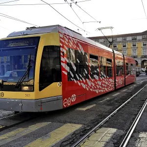 A modern red and yellow tram on rails in front of a historic building in a city center