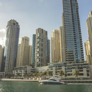 Modern skyscrapers and a boat on a city waterway under the sun