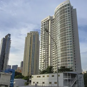 Modern skyscrapers rise into the sky of a city surrounded by trees and clear blue sky Modern skyscrapers rise into the sky of a city surrounded by trees and clear blue sky