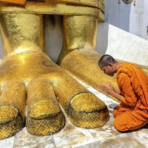 Monk praying at the feet of the golden Buddha statue of Wat Intharawihan